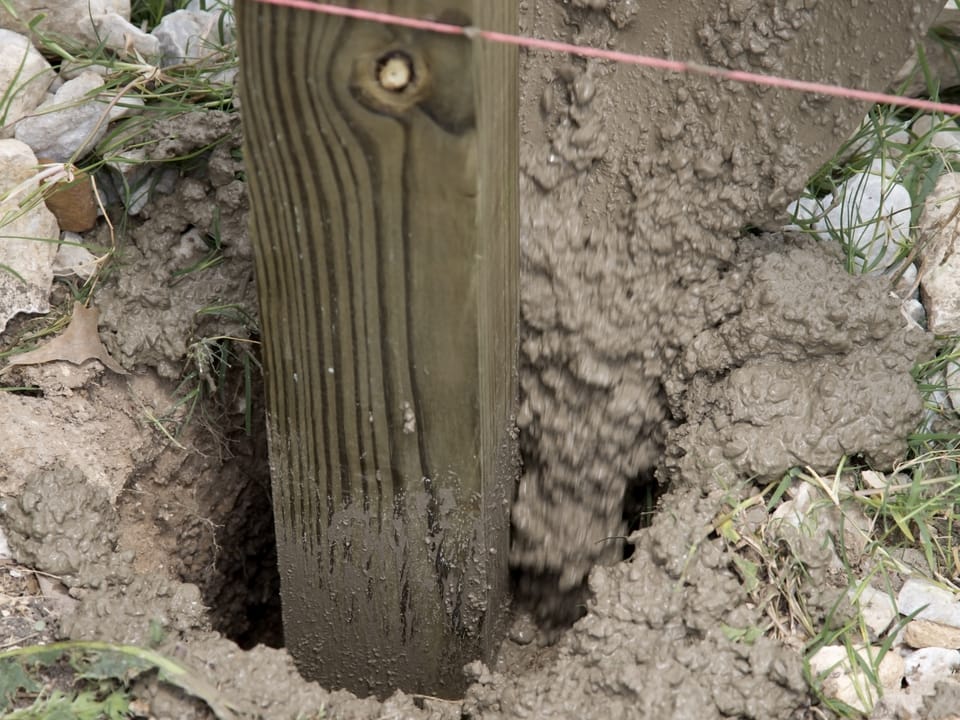 New wood fence post being set in fresh concrete